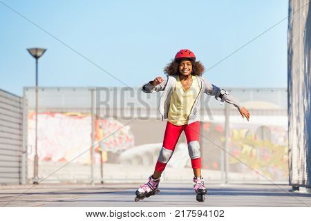 Portrait of preteen African girl, happy inline skater, exercising at outdoor rollerdrom