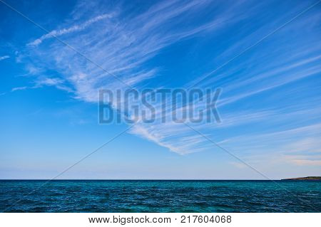 Simple blue sky with diagonal stripes of clouds over the sea