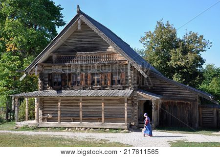 A woman in national Russian clothes goes to a traditional Russian ancient wooden house.