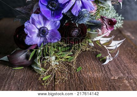 growing, decoration, romance concept. on the wooden table there is adorable bouquet of flowers, wonderful maroon battercup is surrounded with lilac abemons