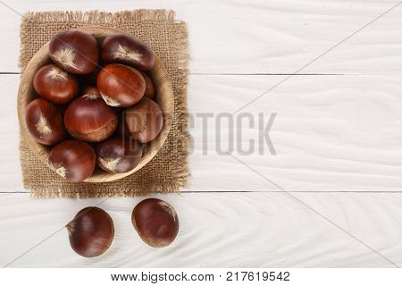 chestnut in bowl on white wooden background with copy space for your text. Top view. Flat lay.