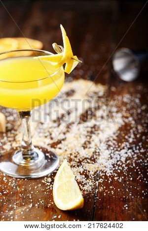 glass with yellow lemon cocktail on the bar on a black background. the cocktail is decorated with lemon zest