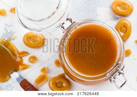 Homemade salted caramel sauce in a glass jar on stone table