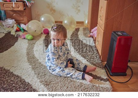 Young blond girl in a children's room sits next to a thermal electric appliance in the children's room