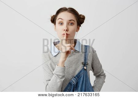 Woman with polite facial expressions looking on camera holding index finger on lips. Female housewife asking to keep silence in order to not disturb her children while sleeping. Gestures, reactions