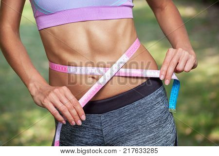 Slim girl bodybuilder centimeter measuring her waist in a gym. Sports concept fat burning and a healthy lifestyle.