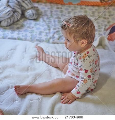 Baby girl blonde in children's room plays on a large bed
