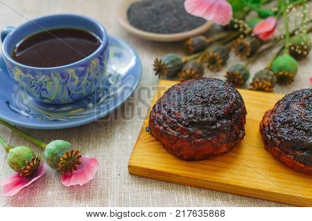 Sweet bun with flax seed and poppy and cup of tea on table.