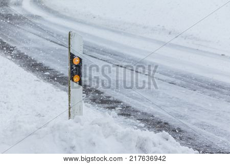 Reflector post at snowy slippery icy white snow winter road. The street track is slick and frozen. High dangerous risk of an accident through the blizzard snowstorm and severe weather at christmas time season.