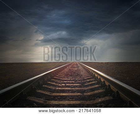 rails going away to the dark rainy clouds. gloomy landscape. Black and white image with rails going away into the dark sky landscape
