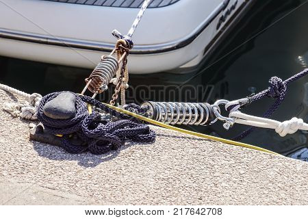 Metal cleat for mooring boats, bolted to the ground, with rope and shock absorber spring .