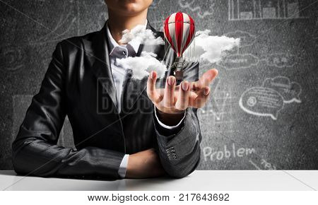Closeup of business woman in suit presenting flying aerostate among clouds in her palm with business sketches on background. 3D rendering.