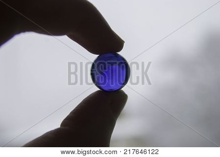 Look to inverted world through the blue glass ball in fingers.