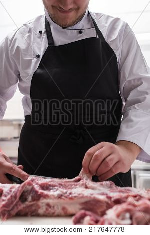 Restaurant chef in black apron cutting fresh lamb meat in the kitchen. Ingredient preparation before cooking a delicious meal