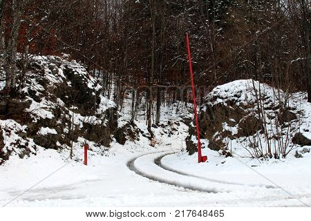Open gate entrance on snow covered forest road blocked by red metal ramp with fresh tire tracks on white snow with forest trees background