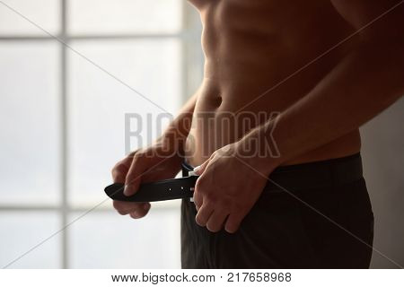Man unbuckling belt. Attractive male body close up.