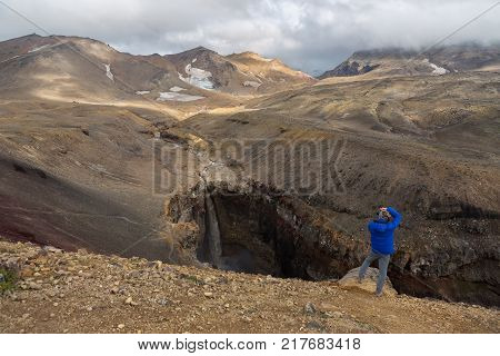 Kamchatka Peninsula, Russia - August 26, 2016: Tourist is taking pictures of a waterfall in a Dangerous Canyon near Mutnovsky volcano in Kamchatka.