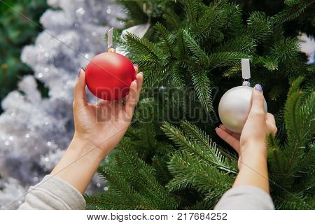 Closeup view of hands decorating Christmas tree with decoration balls. difficult decision.