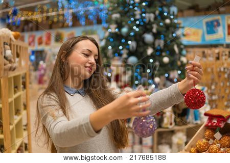 beautiful customer girl choosing Christmas tree decoration balls. difficult decision. Various choice