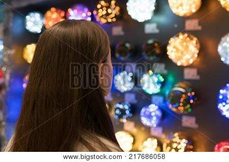 Cheerful happy customer girl choosing Christmas tree decorations - garlands. difficult decision. Various choice