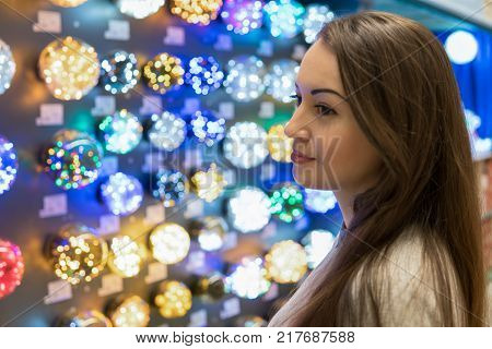 Cheerful happy customer girl choosing Christmas tree decorations - garlands. difficult decision. Various choice