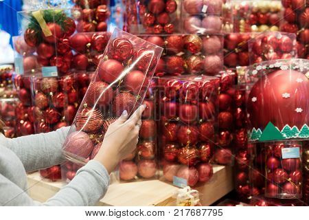 closeup view of customer girl hands taking red Christmas tree decoration balls. difficult decision. Various choice