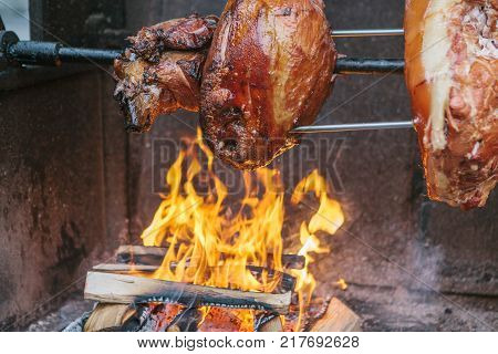 Large chunks of delicious pork hams cooked on an open fire. The street food. Food outdoors. Camping and cooking on a spit over the fire. Camping.