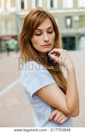 young thoughtfull redhead female in a gray shirt walking around city. Concept of modern freedom hipster human, close up portrait