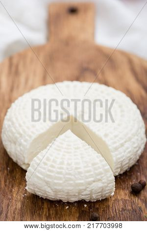 Sliced round white homemade cheese - traditional milk creamy dairy product on vintage wooden board. Rustic style.