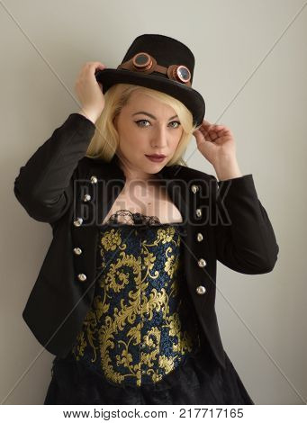 Young Steampunk girl holds hat with goggles and elaborate corset looking directly at viewer