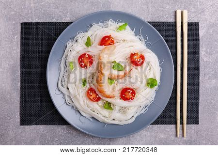 A top view on a chinese food. Chopsticks, shrimps and tomatoes on a rise nuddles on the marble background. Close-up of objects. Food concept.