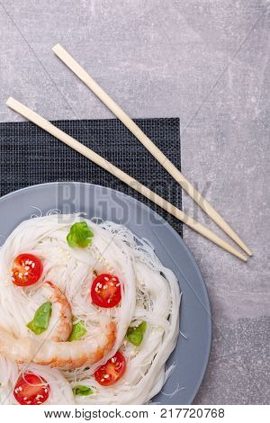 A top view on a chinese food. Chopsticks, shrimps and tomatoes on a rise nuddles on the marble background. Close-up of objects. Food concept.