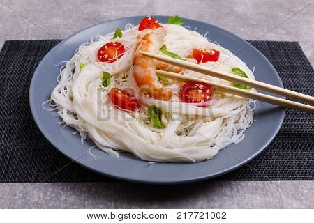A top view on a chinese food. Chopsticks, shrimps and tomatoes on a rise nuddles on the marble background. Close-up of objects. Food concept.