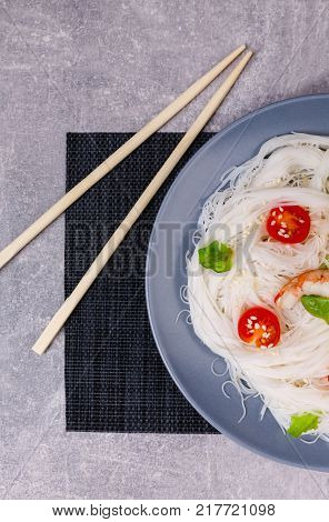 A top view on a chinese food. Chopsticks, shrimps and tomatoes on a rise nuddles on the marble background. Close-up of objects. Food concept.