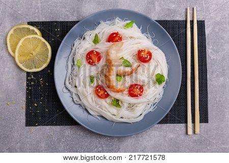 A top view on a chinese food. Chilli, chopsticks, shrimps and tomatoes and lemon on a rise nuddles on the marble background. Close-up of objects. Food concept.