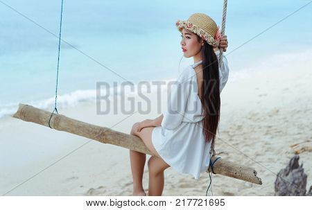 Single woman sitting on swing at beach with wearing white dress relaxing vacation and resting on summer season lonely,alone,solitude lifestyle in tropical blue sea
