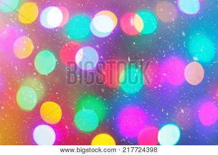Defocused colorful ligths of Christmas tree. Multicolored bokeh lights during a snowfall. Background for greeting card. Winter composition. Happy holiday mood. Xmas and New Year fairy tale wallpaper.