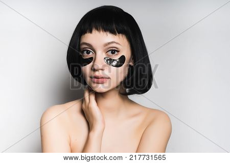attractive young girl with black hair looks at the camera, under the eyes of cheny silicone patches