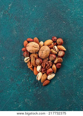 Nuts heap in heart shape on green cement background. Heart shape made of multiple different nuts and seeds mix. Copy space for text. Top view or flat-lay.