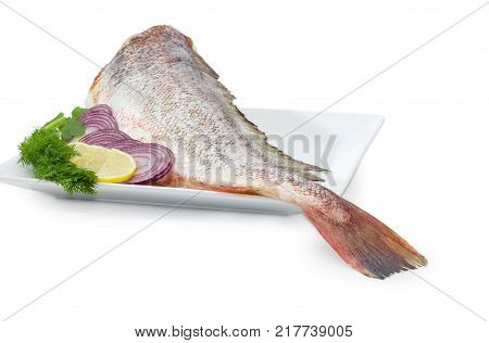 Uncooked red cod without head dill twig sliced lemon and red onion on the large square dish at shallow depth of field on a white background