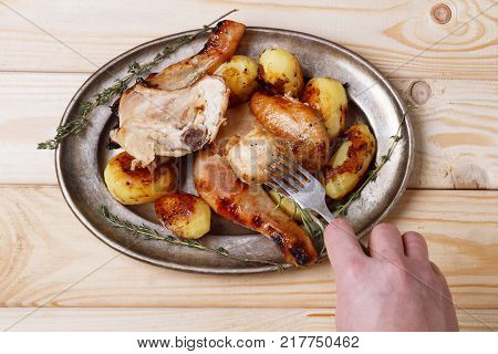 hand with fork against roasted chicken with potatoes.