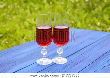 Two Glasses With Homemade Red Wine On Blue Boards Outdoors In Countryside At Summer.