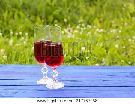 Two Glasses With Homemade Red Wine On Blue Boards Outdoors In Countryside At Summer.