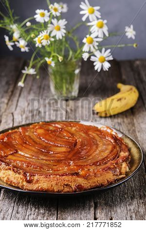 Traditional homemade banana caramel pie on vintage wooden table decorated a bouquet of chamomiles.  Upside down banana cake. Selective focus