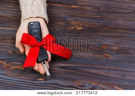Car key with red bow in woomen hand on wooden background. Valentine's Day concept.