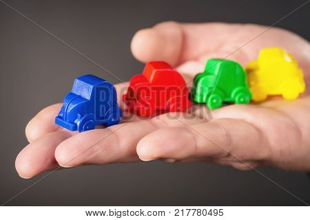 Toy cars in the colors blue red green and yellow are carried on a palm.