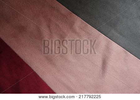 Diagonally sewn pieces of grey pink and red artificial suede