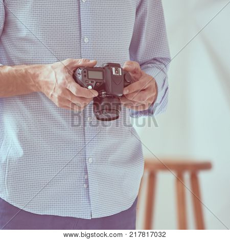 Closeup of male photographer checking modern camera, focus is on hand with camera, image with vintage toning
