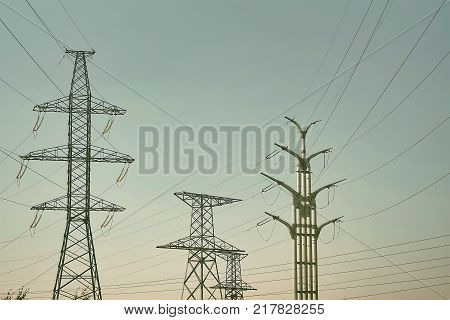 Several High metal towers. Power line with conductors against the sky. City, industrial district at dawn