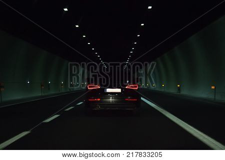A black passenger car rides in a long tunnel